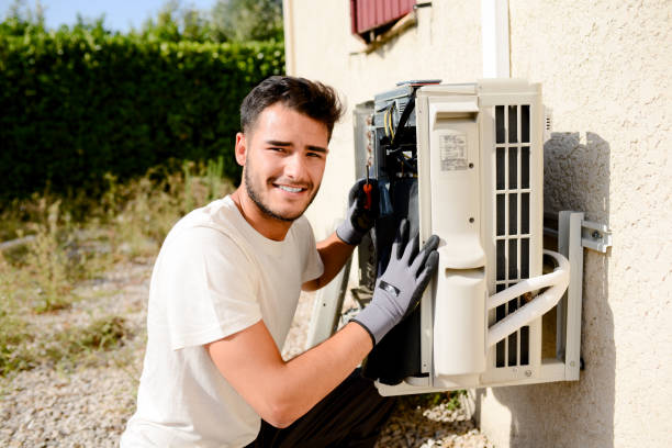 young man electrician installer working on outdoor compressor unit air conditioner at a client's home